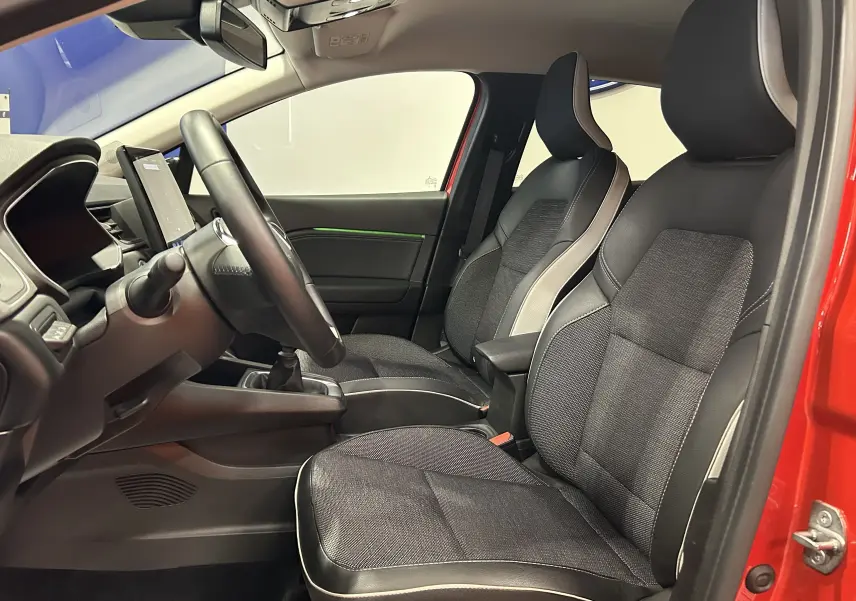 Intérieur avant du Renault Captur rouge flamme 2024, sièges tissu noir avec surpiqûres claires et volant visible côté gauche.