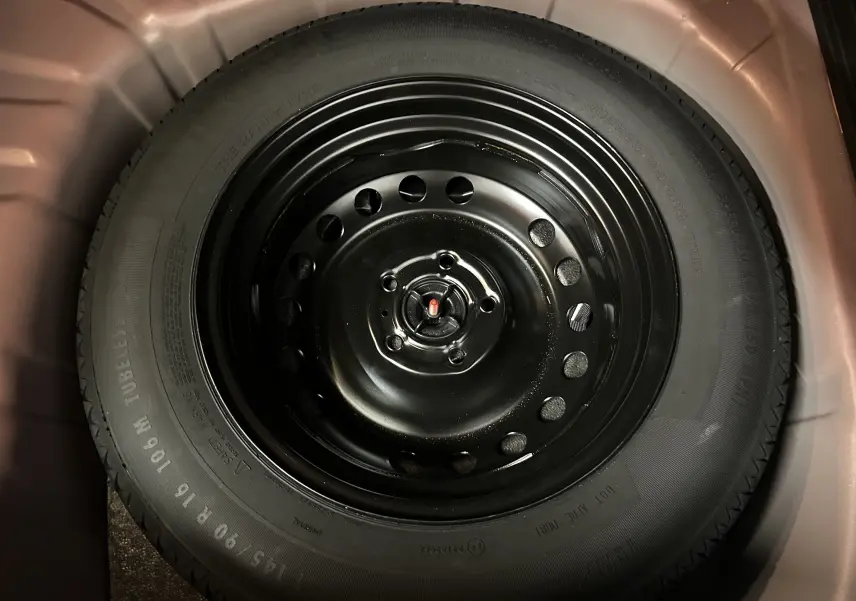 Roue de secours noire en acier du Renault Captur TCE 90CH TECHNO 2024, vue en gros plan dans le coffre.