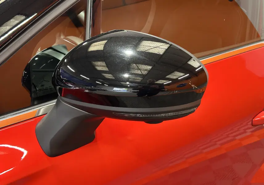 Rétroviseur noir brillant côté gauche du Renault Captur rouge flamme métal 2024 avec intérieur marron visible.