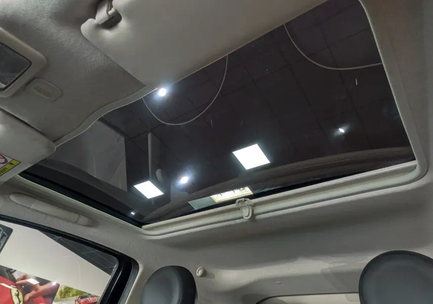 Toit panoramique ouvert vu de l'intérieur d'une Fiat 500 1.2 69 CH Lounge noire, sièges avant visibles.