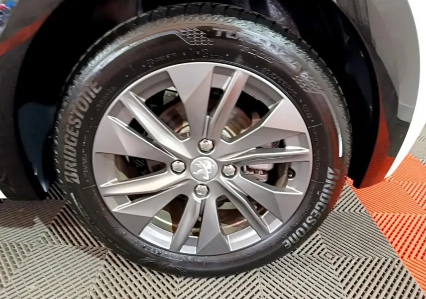 Gros plan sur la roue avant droite avec jante alliage argentée et pneu Bridgestone d'une Peugeot 208 blanche électrique.