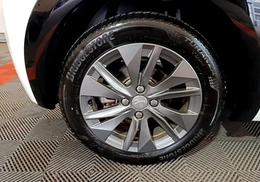 Gros plan sur la roue avant droite d'une Peugeot 208 électrique blanche, jante alliage gris argenté et pneu Bridgestone.