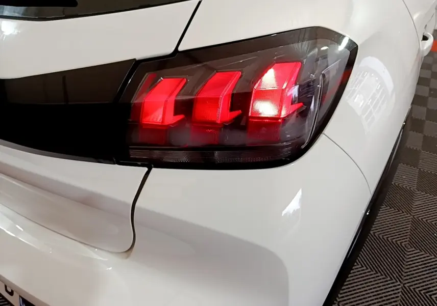 Gros plan sur le feu arrière droit rouge d'une Peugeot 208 électrique blanche, avec carrosserie brillante et détails noirs.