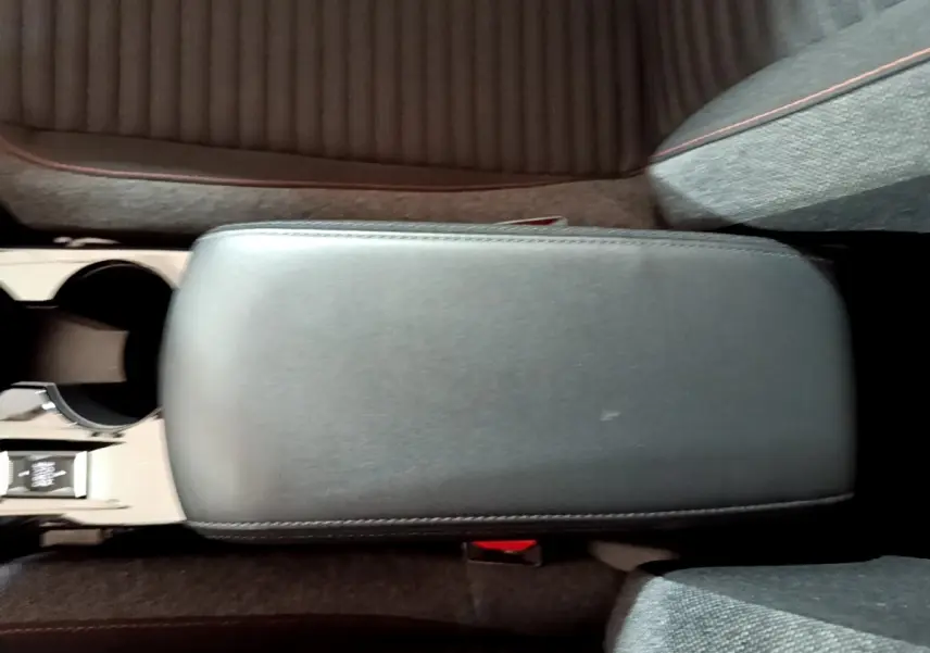 Vue plongeante sur l'accoudoir central noir et les sièges tissu gris de la Peugeot 208 électrique blanche.