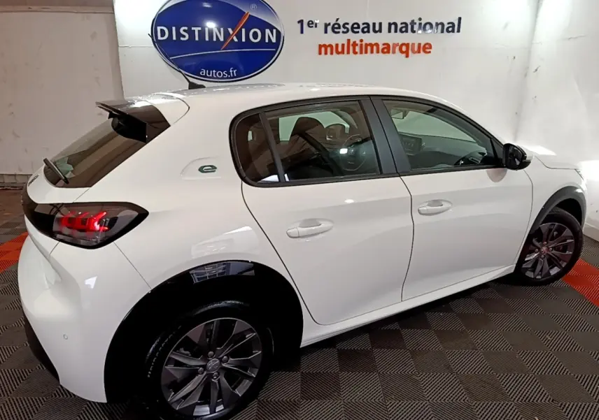 Vue 3/4 arrière droite d'une Peugeot 208 électrique Active Business blanche avec jantes foncées et logo "e" vert sur l'aile arrière.