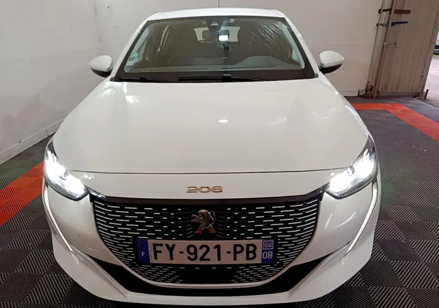 Vue frontale d'une Peugeot 208 électrique blanche avec phares LED allumés et calandre noire distinctive.