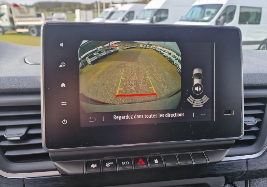 Écran multimédia montrant la caméra de recul du Nissan Primastar blanc, vue arrière avec lignes de guidage colorées.