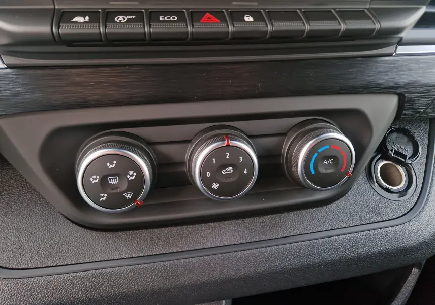 Gros plan sur les commandes de climatisation du Nissan Primastar blanc 2025, avec boutons rotatifs et prise 12V visible.