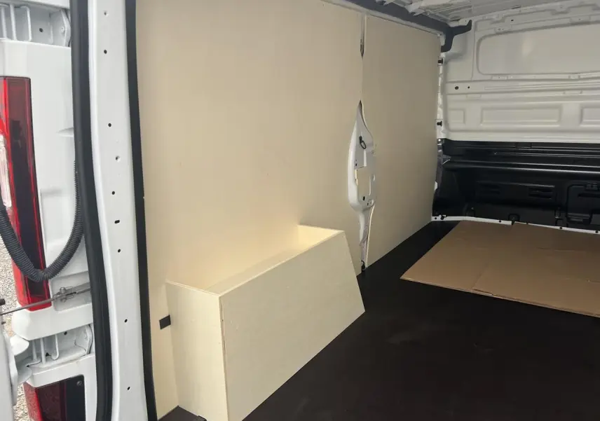 Vue intérieure arrière du Nissan Primastar blanc 2025, montrant le revêtement bois clair du coffre et des parois du compartiment cargo.