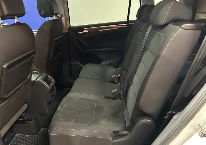 Vue latérale intérieure des sièges arrière noirs en tissu du Volkswagen Tiguan Allspace blanc, avec accoudoirs et ceintures visibles.