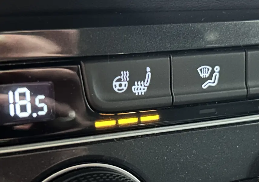 Gros plan sur les commandes de chauffage du volant et siège chauffant du Volkswagen Tiguan Allspace blanc, affichant 18,5°C.