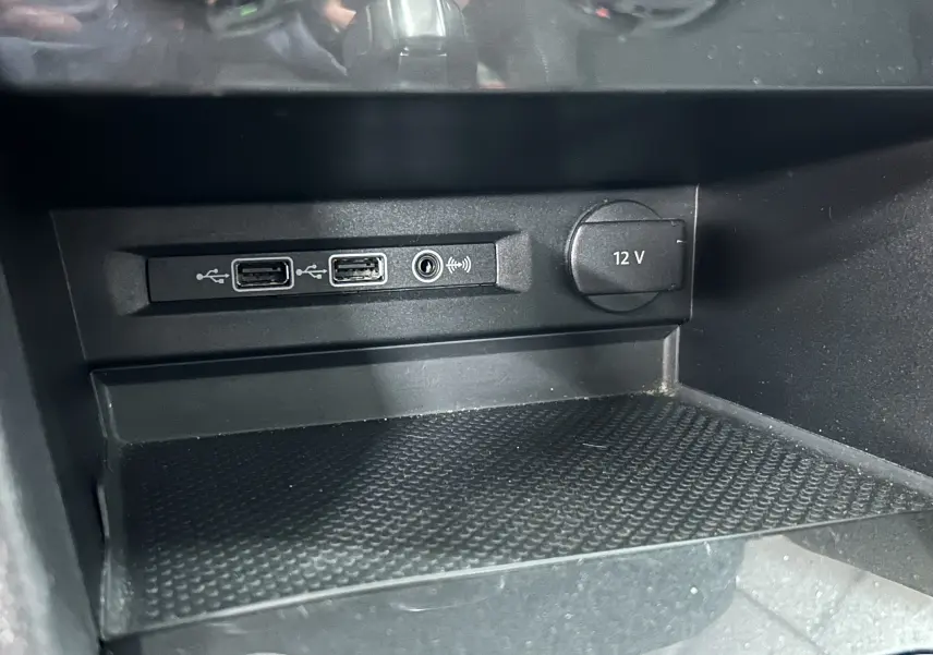 Prise 12V et ports USB visibles dans la console centrale d'un Volkswagen Tiguan Allspace blanc, vue rapprochée intérieure.