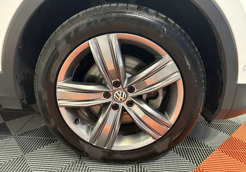 Gros plan sur la roue avant droite du Volkswagen Tiguan Allspace blanc avec jante alliage 5 branches double finition.