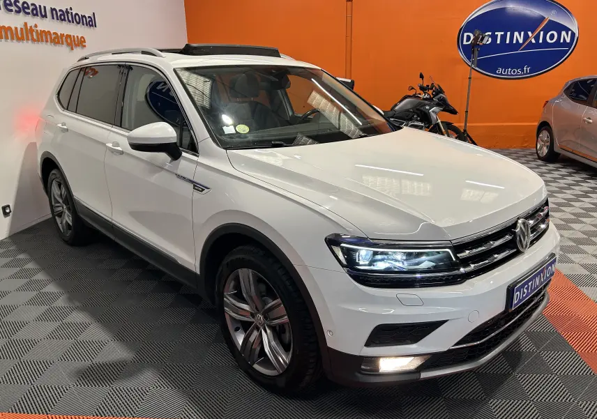 Volkswagen Tiguan Allspace blanc en 3/4 avant droit avec phares LED allumés en intérieur showroom.