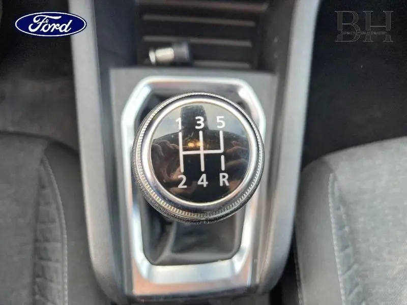 Le levier de vitesse manuel noir avec marquages blancs, entouré de garnitures grises et sièges en tissu noir.