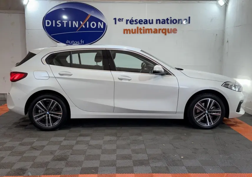 Profil côté gauche d'une BMW Série 1 116i Business Design blanche, avec jantes alliage et feux arrière LED visibles.