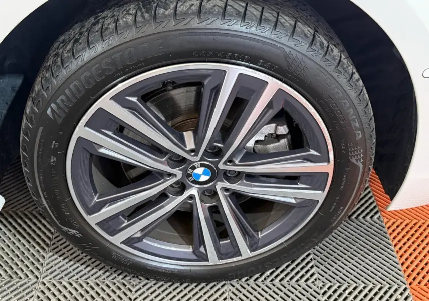 Gros plan sur la roue avant droite d'une BMW Série 1 blanche avec jante alliage bicolore et logo BMW central.