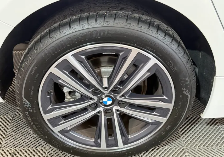 Gros plan sur la roue avant droite d'une BMW Série 1 blanche, avec jante alliage et logo BMW central visible.