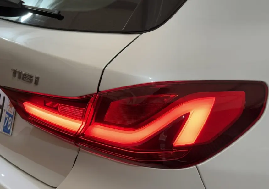 Feu arrière droit allumé sur BMW Série 1 118i blanc, vue rapprochée du coffre et du badge arrière.