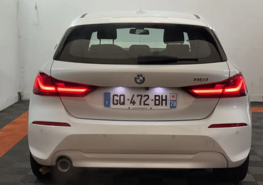 Vue arrière d'une BMW Série 1 116i blanche avec feux LED allumés et plaque d'immatriculation française.