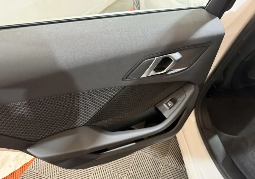 Gros plan sur la porte avant gauche noire avec poignée argentée et bouton de lève-vitre d'une BMW Série 1 blanche 2023.