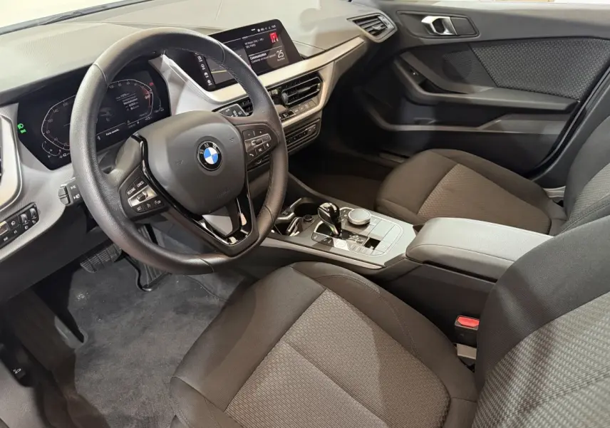 Intérieur de la BMW Série 1 116i 2023 vu côté conducteur, volant cuir et écran tactile 10,25 pouces visibles.