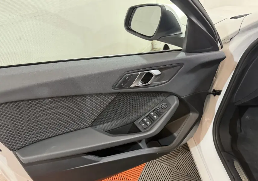 Vue intérieure de la porte avant gauche d'une BMW Série 1 blanche, avec commandes électriques et garniture textile.