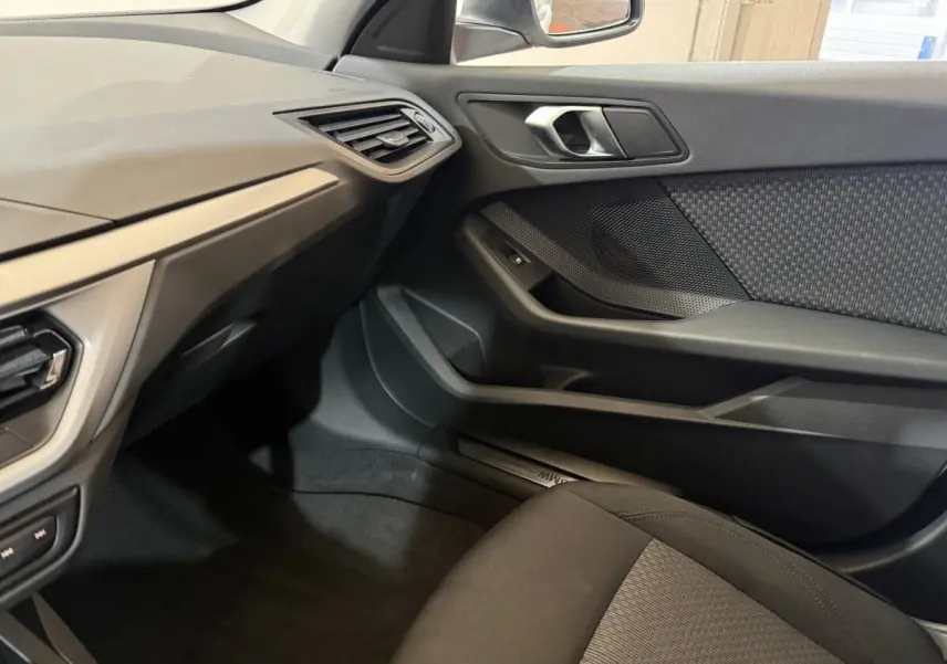 Intérieur côté passager de la BMW Série 1 116i blanc, montrant la porte et le tableau de bord noir avec détails tissu.