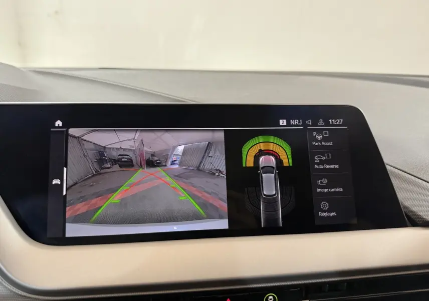 Écran tactile central de la BMW Série 1 blanche 116i DKG7 montrant l'aide au stationnement arrière en intérieur.