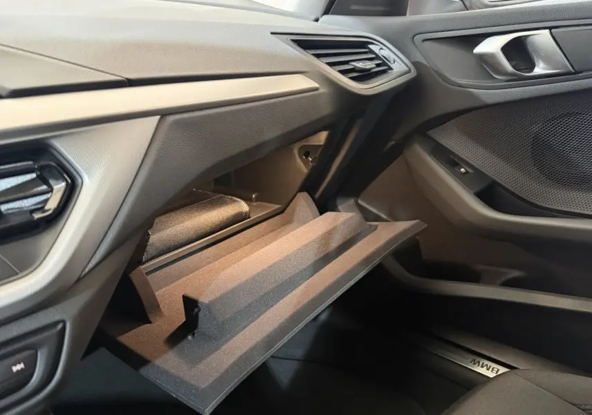 Intérieur BMW Série 1 116i 2023, vue côté passager sur boîte à gants ouverte et tableau de bord noir.