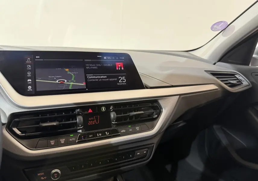 Tableau de bord de BMW Série 1 116i blanc, vue intérieure côté passager avec écran tactile et commandes climatisation.