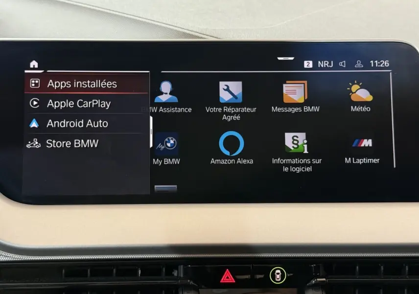 Écran tactile central de 10,25 pouces affichant les applications connectées dans l’habitacle beige d’une BMW Série 1 blanche.