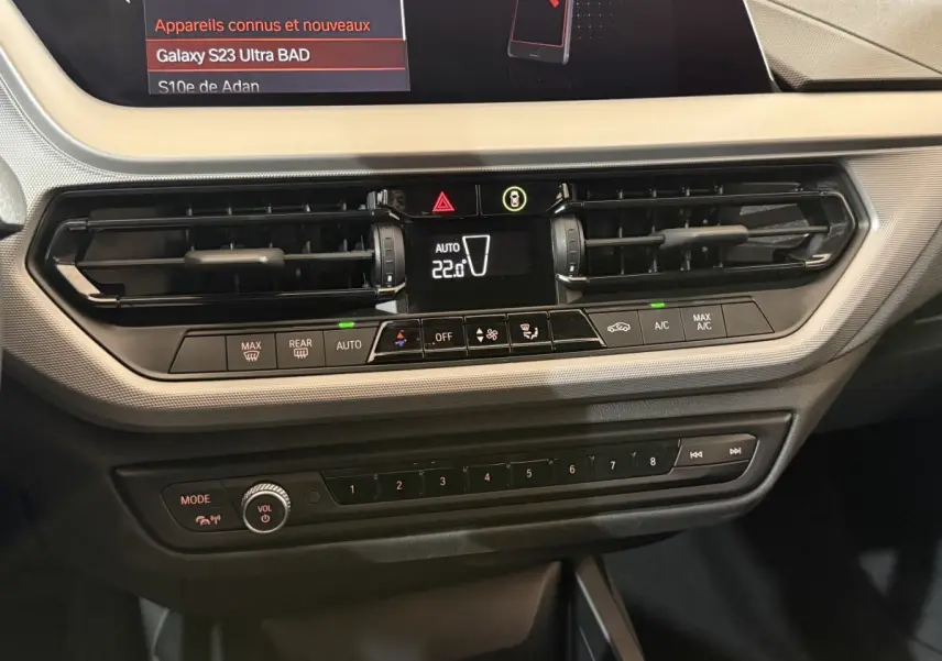 Vue rapprochée du tableau de bord noir de la BMW Série 1 116i 2023 avec commandes climatisation et écran tactile.