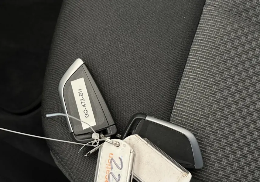 Gros plan sur une clé BMW noire et argent posée sur un siège tissu gris foncé à motifs.