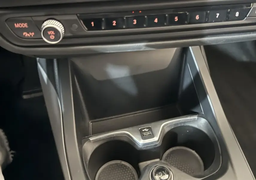 Gros plan sur la console centrale noire de la BMW Série 1 116i avec porte-gobelets et commandes audio visibles.