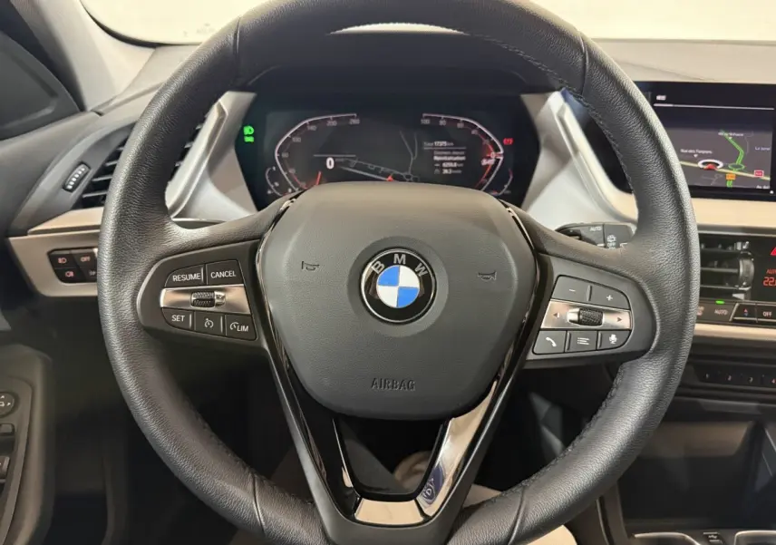 Vue rapprochée du volant cuir noir de la BMW Série 1 116i 2023 avec tableau de bord digital et écran tactile.