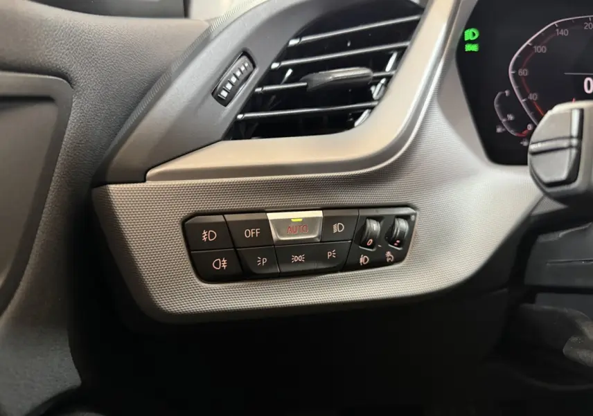 Gros plan sur le tableau de bord côté gauche d'une BMW Série 1 blanche, montrant les commandes d'éclairage avec réglage automatique.