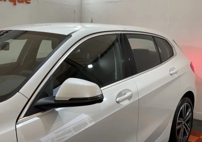 Vue latérale côté gauche d'une BMW Série 1 116i blanche avec rétroviseur et poignées de porte visibles.