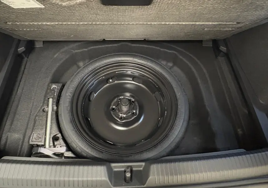 Vue plongeante sur la roue de secours compacte noire et le cric dans le coffre d'une Volkswagen Golf 2.0 TDI 150 DSG7.