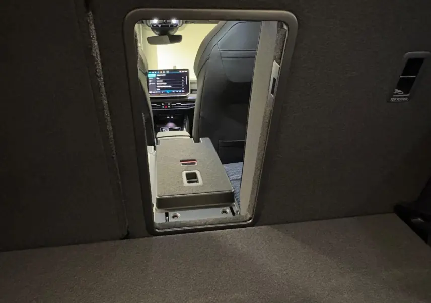 Vue intérieure depuis le coffre vers l'avant, montrant l'ouverture du siège arrière et l'écran tactile du tableau de bord.