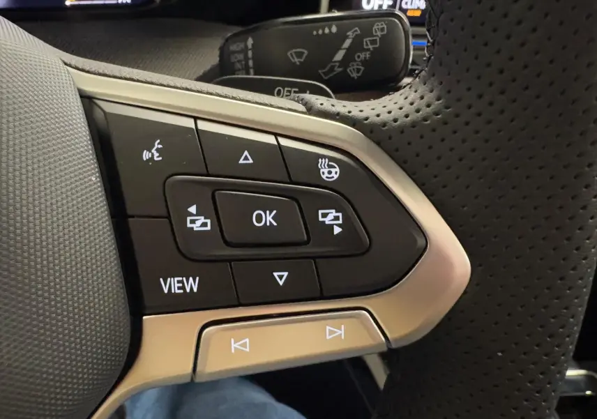 Gros plan sur les commandes multifonctions en cuir perforé du volant de la Volkswagen Golf noire, avec boutons rétroéclairés.