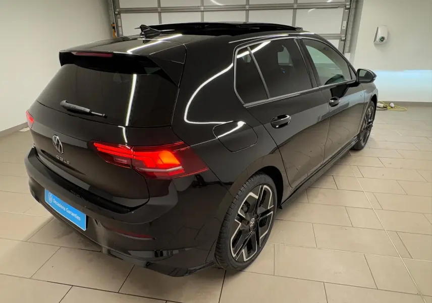 Vue 3/4 arrière droite d'une Volkswagen Golf 2.0 TDI R-Line noire Grenadille avec toit ouvrant panoramique en intérieur showroom.