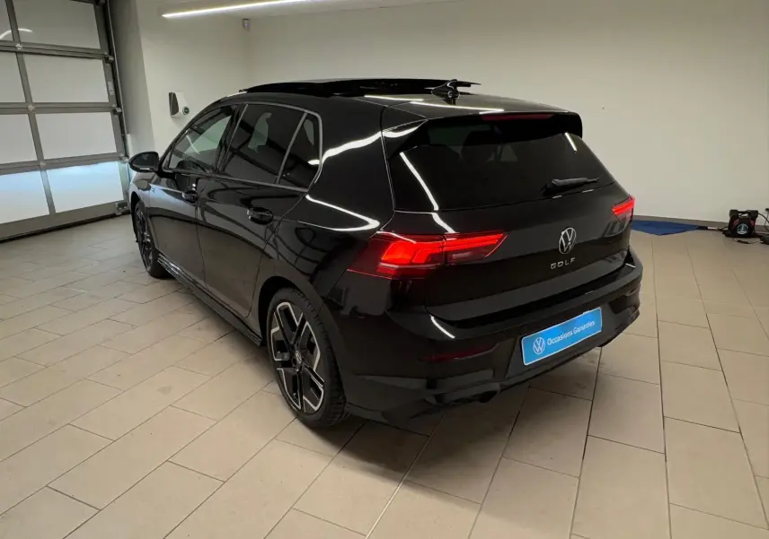 Vue 3/4 arrière droite d'une Volkswagen Golf 2.0 TDI R-Line noir grenadille avec feux arrière allumés en intérieur.