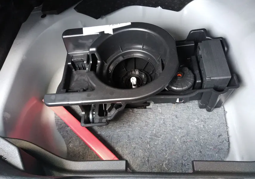 Gros plan sur le rangement sous le plancher du coffre d’un Jeep Avenger gris, montrant un support d’outils noir.