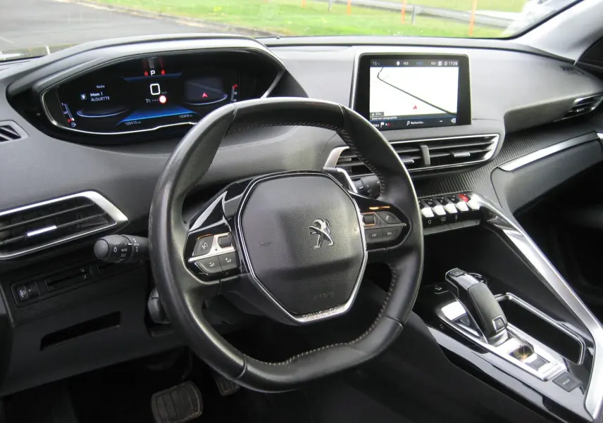 Vue intérieure du poste de conduite du Peugeot 3008 noir, avec volant compact, tableau de bord digital et écran tactile central.