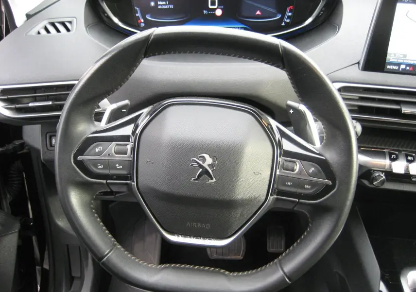 Volant cuir noir avec commandes intégrées et logo Peugeot visible, tableau de bord numérique en arrière-plan du Peugeot 3008 Business 2020.