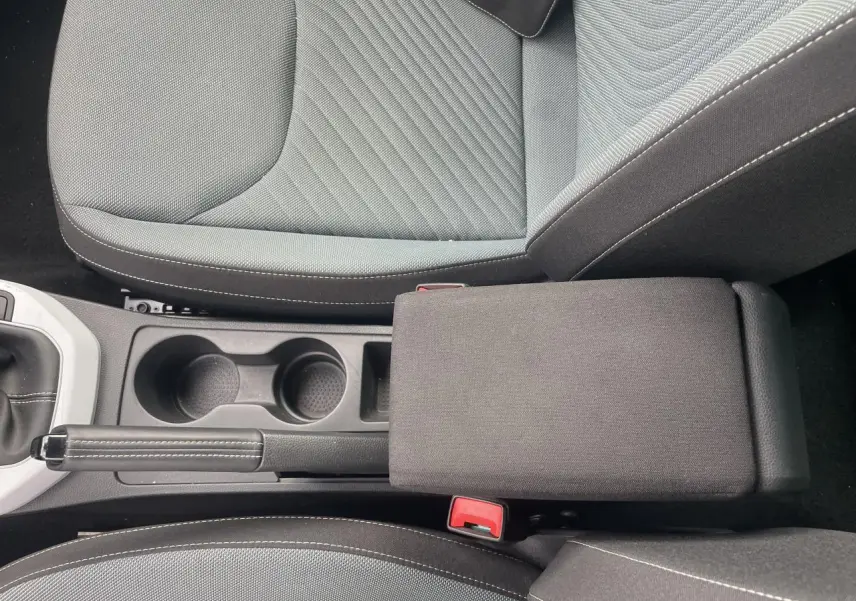 Vue plongeante sur l'accoudoir central et les sièges gris foncé avec coutures blanches d'une SEAT IBIZA blanche 2025.