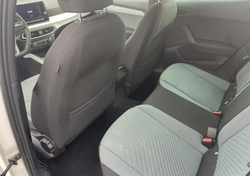 Vue intérieure arrière gauche de la SEAT IBIZA blanche 2025, sièges tissu bicolore et tableau de bord digital visible.