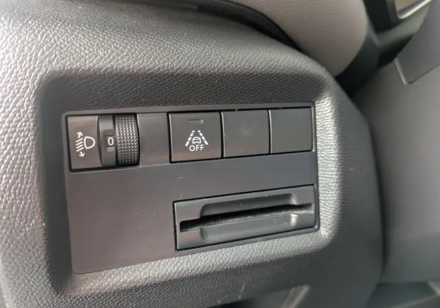 Gros plan sur les commandes noires du tableau de bord côté conducteur du Citroën C5 Aircross blanc, avec réglage des phares et bouton d'assistance.