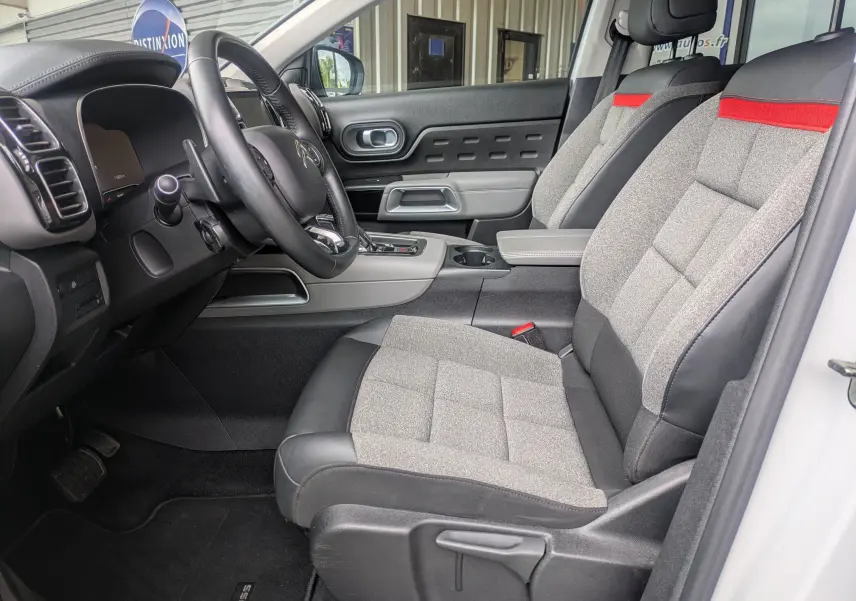Vue intérieure côté conducteur du Citroën C5 Aircross blanc 2020, sièges tissu gris avec bande rouge et volant cuir noir.